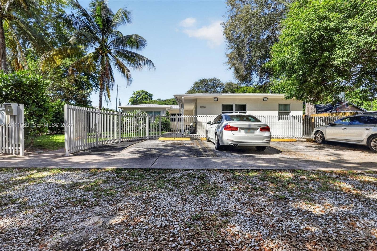 12800 NE 11th Avenue, #4, North Miami, North Miami, FL 33161 Single-story exterior featuring a concrete facade, paved parking area, metal fencing, and mature landscaping