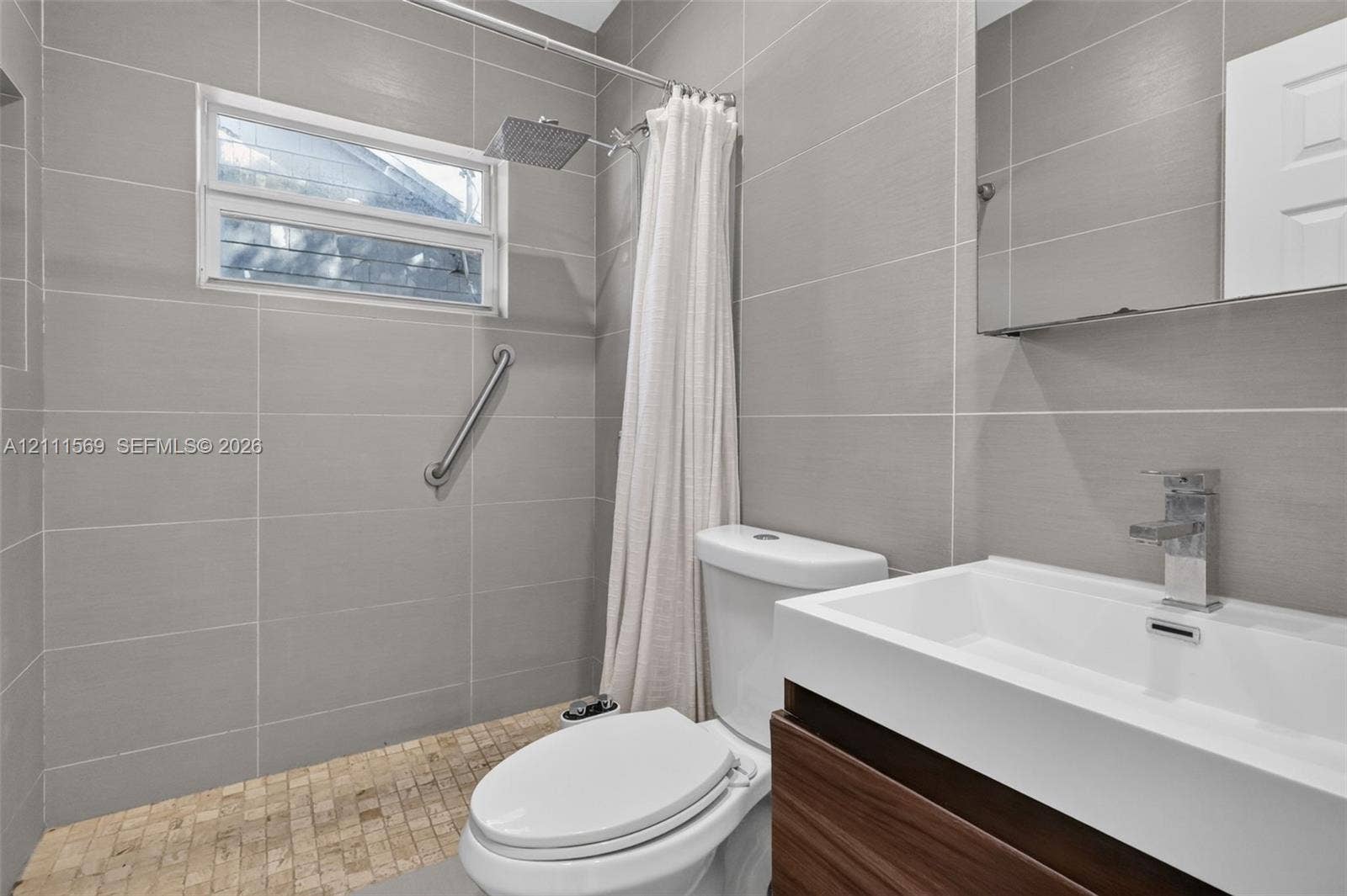 12800 NE 11th Avenue, #4, North Miami, North Miami, FL 33161 Bathroom featuring large-format gray wall tile, wood-finish vanity with an integrated rectangular sink, wall-mounted rain shower head, and textured stone floor tile