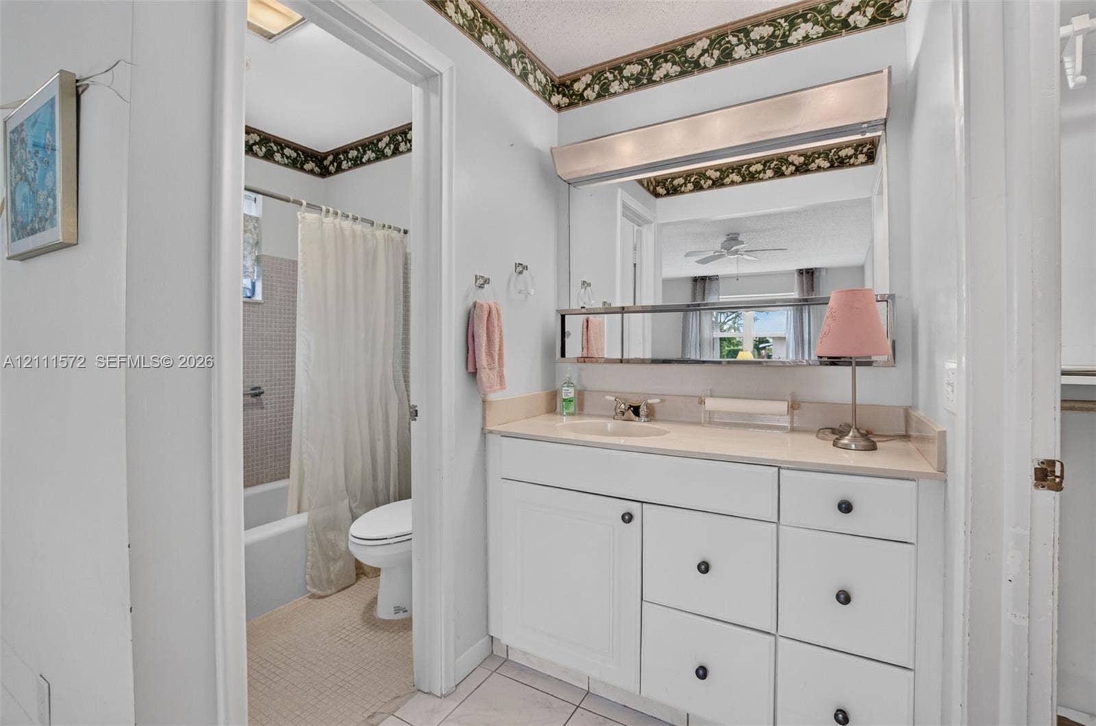 Bathroom featuring a white vanity cabinet with multiple storage drawers, a light-toned countertop with an integrated sink, a full-width vanity mirror, and a tile-surround soaking bathtub