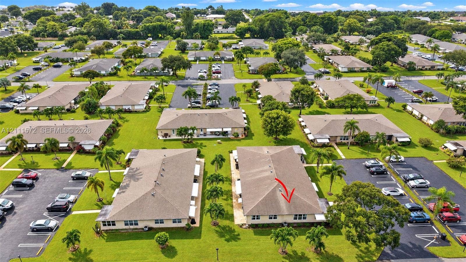 Aerial perspective of a multi-unit residential property featuring low-pitched shingle roofing, paved surface parking, and mature palm landscaping