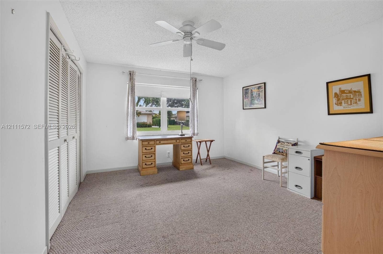 Room featuring wall-to-wall berber carpeting, louvered bi-fold closet doors, a ceiling fan, and a large impact windows providing natural light, energy efficiency