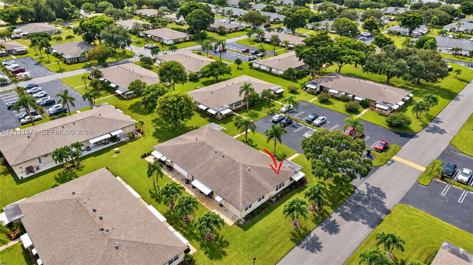 Aerial perspective of a single-story residence featuring a hipped roof, light-colored exterior finish, integrated awnings, and landscaped grounds with mature palm trees