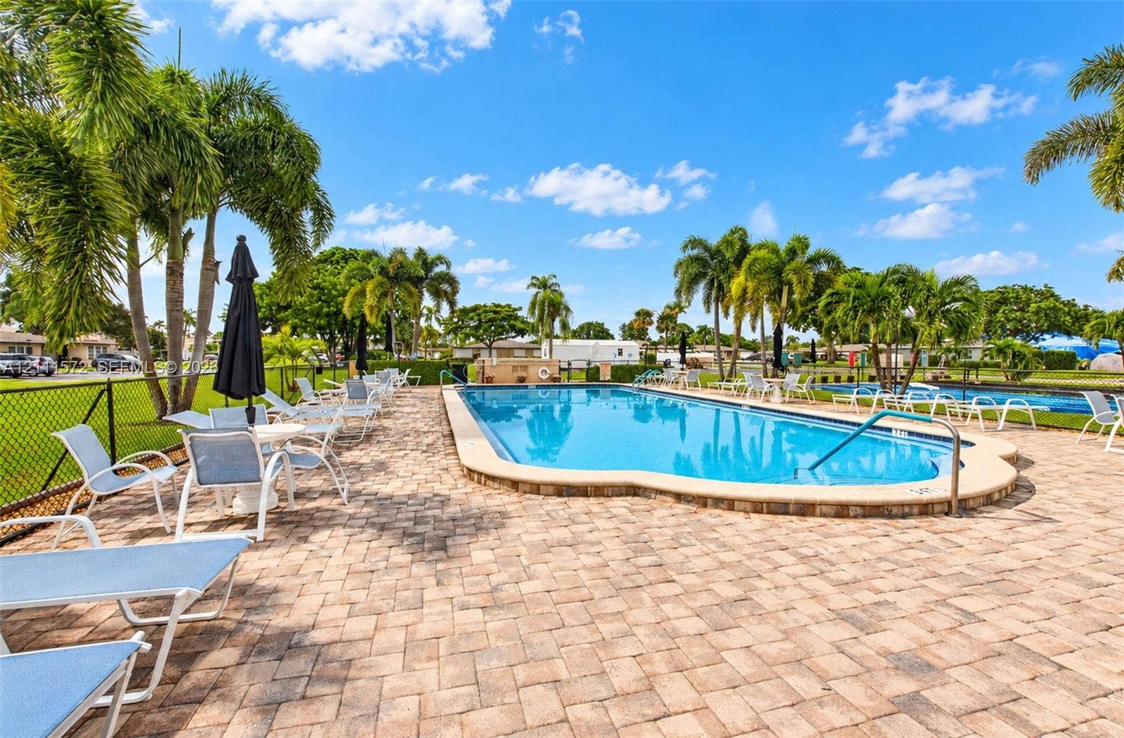 In-ground heated swimming pool featuring a brick-paver deck, and surrounding mature palm trees