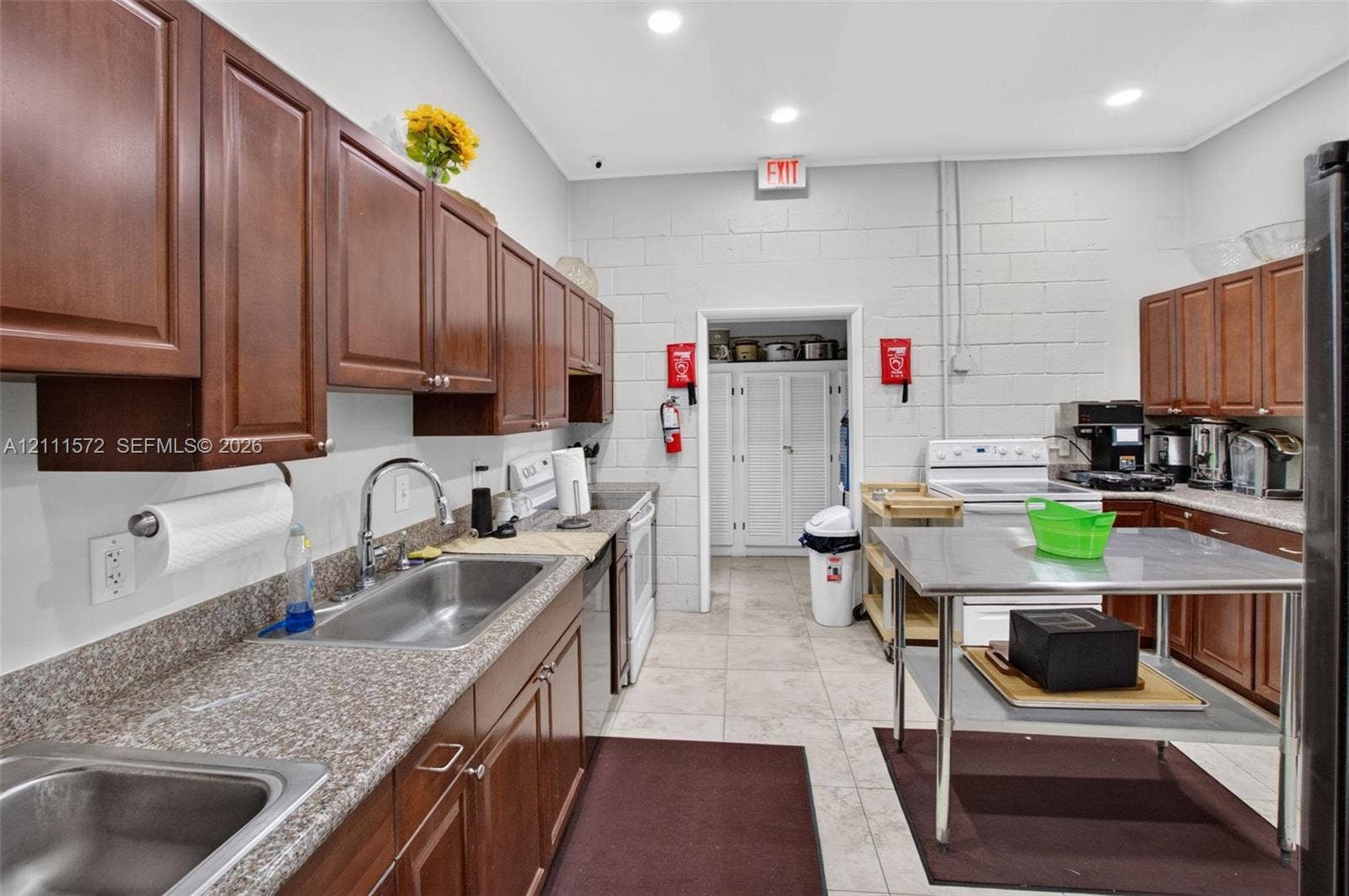 Kitchen featuring wood cabinetry, solid-surface countertops, dual stainless steel sinks with a gooseneck faucet, tile flooring, and recessed lighting