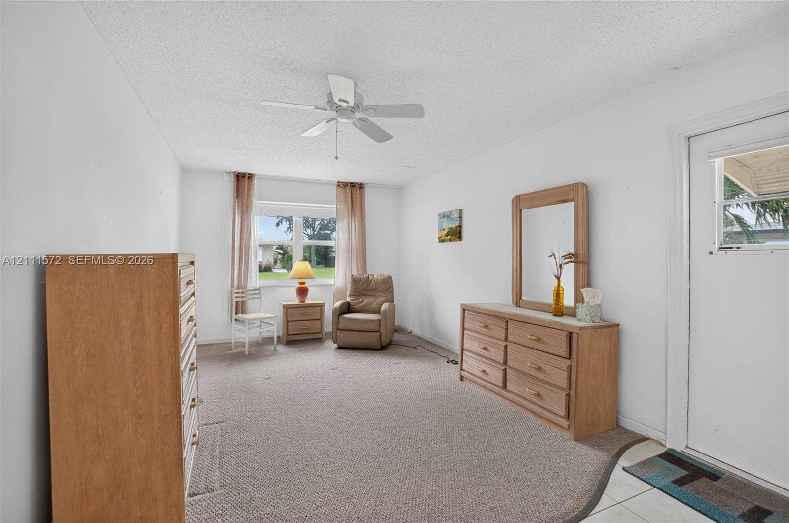 Primary bedroom with berber carpeting, a central ceiling fan, and large impact windows providing natural light, energy efficiency, and sound proofing