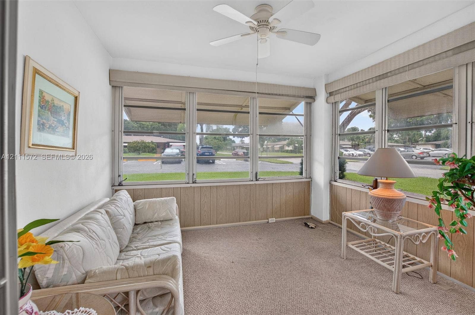 Enclosed sunroom featuring expansive paneled windows, berber carpeting, and a ceiling fan