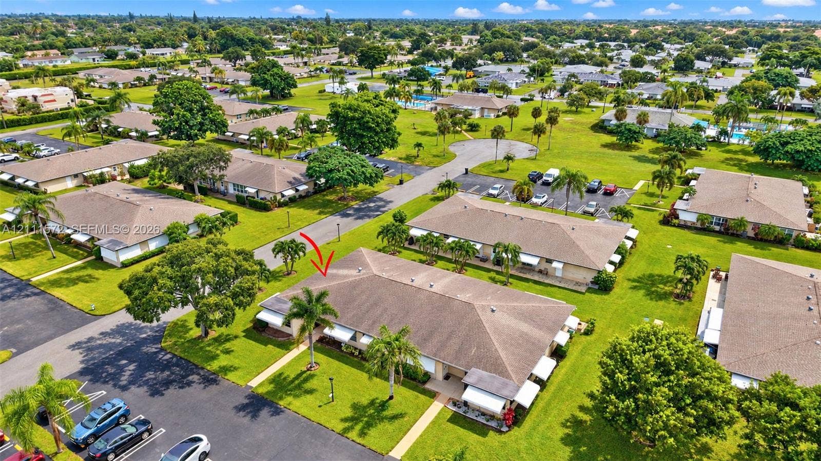Aerial perspective of a single-story residence featuring a hip roof, exterior awnings, and established tropical landscaping. Amenities are just past the cul de sac.