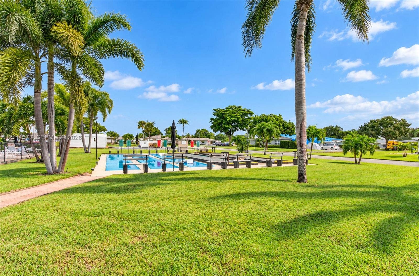 Swimming pool with concrete decking surrounded by expansive lawn, mature palm trees, and perimeter fencing