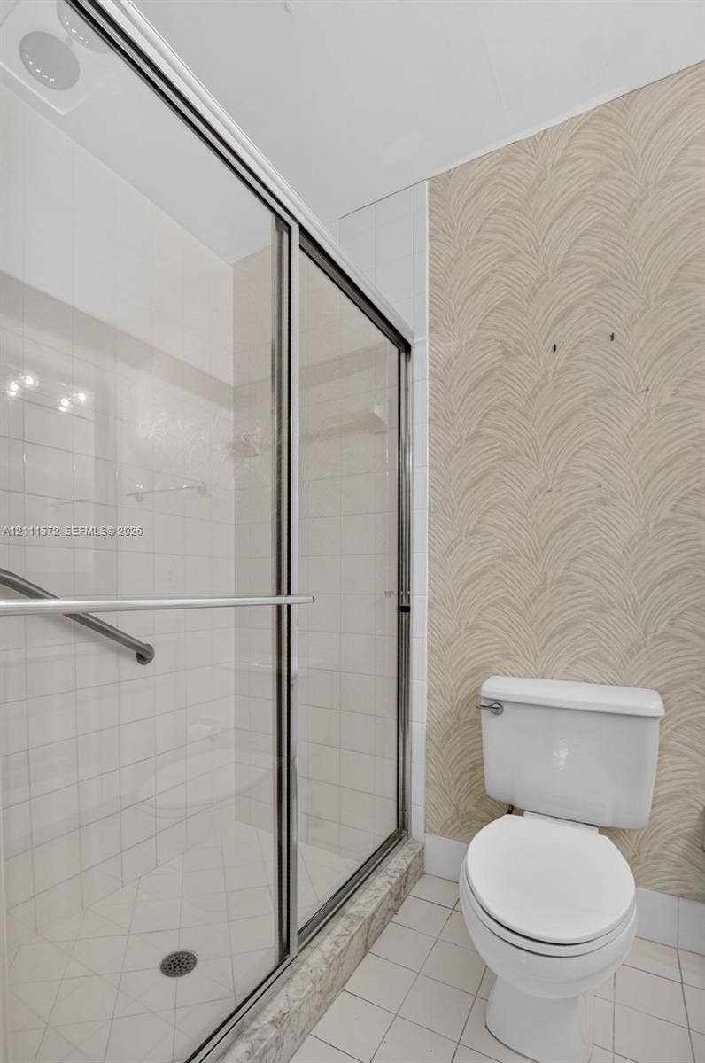 Walk-in shower enclosure featuring a metal-framed glass sliding door, tiled surround, and grab bar, complemented by patterned wall covering and floor tiles