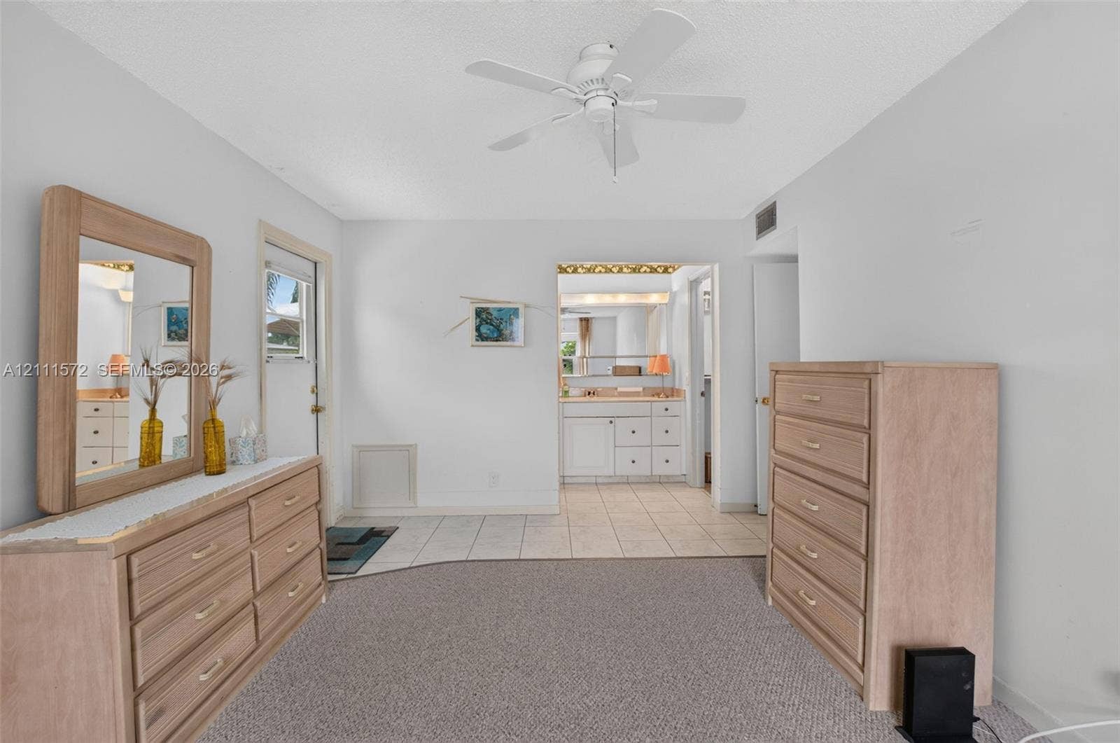 Primary bedroom featuring neutral berber carpeting, ceiling-mounted fan, with tile flooring leading to ensuite bathroom and walk-in closet