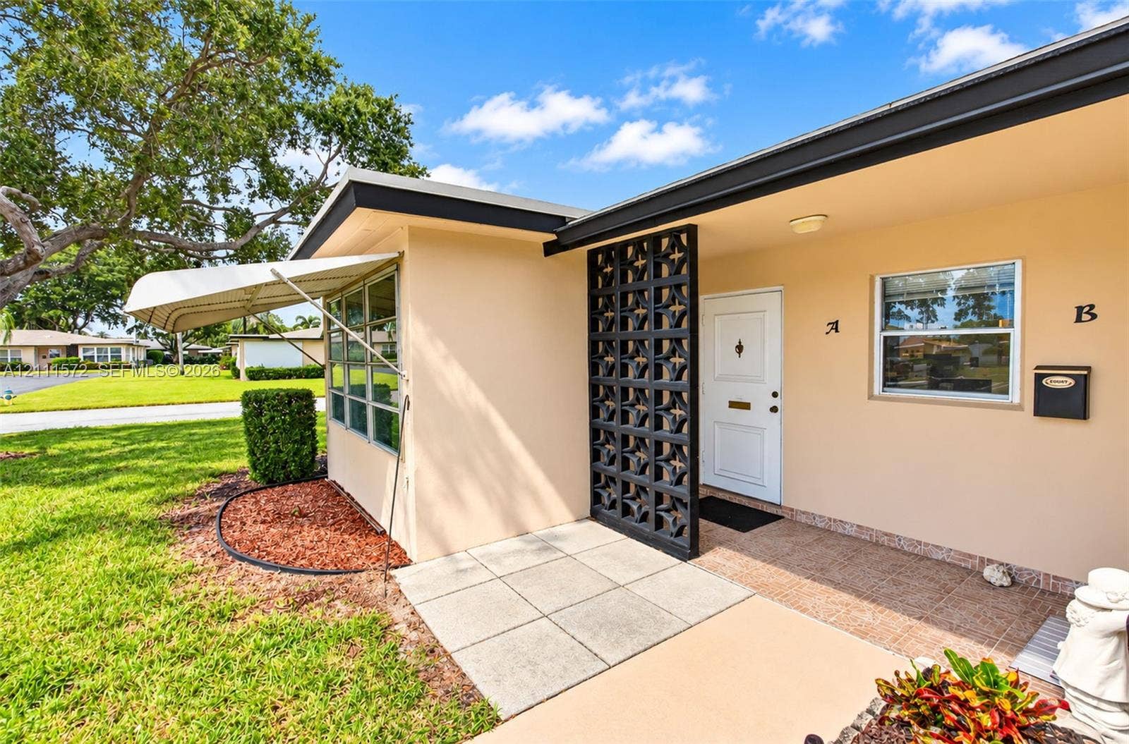 Mid-century modern exterior featuring a decorative breeze block privacy screen, metal window awning, and a paved front patio