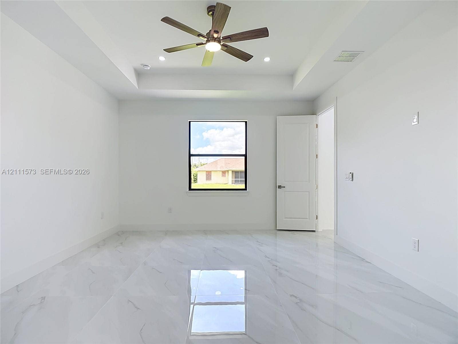 3813 SW 26th Street, Lehigh Acres, FL 33976 Tray ceiling, polished tile flooring with veining, multi-blade ceiling fan with integrated lighting, and dark-framed window