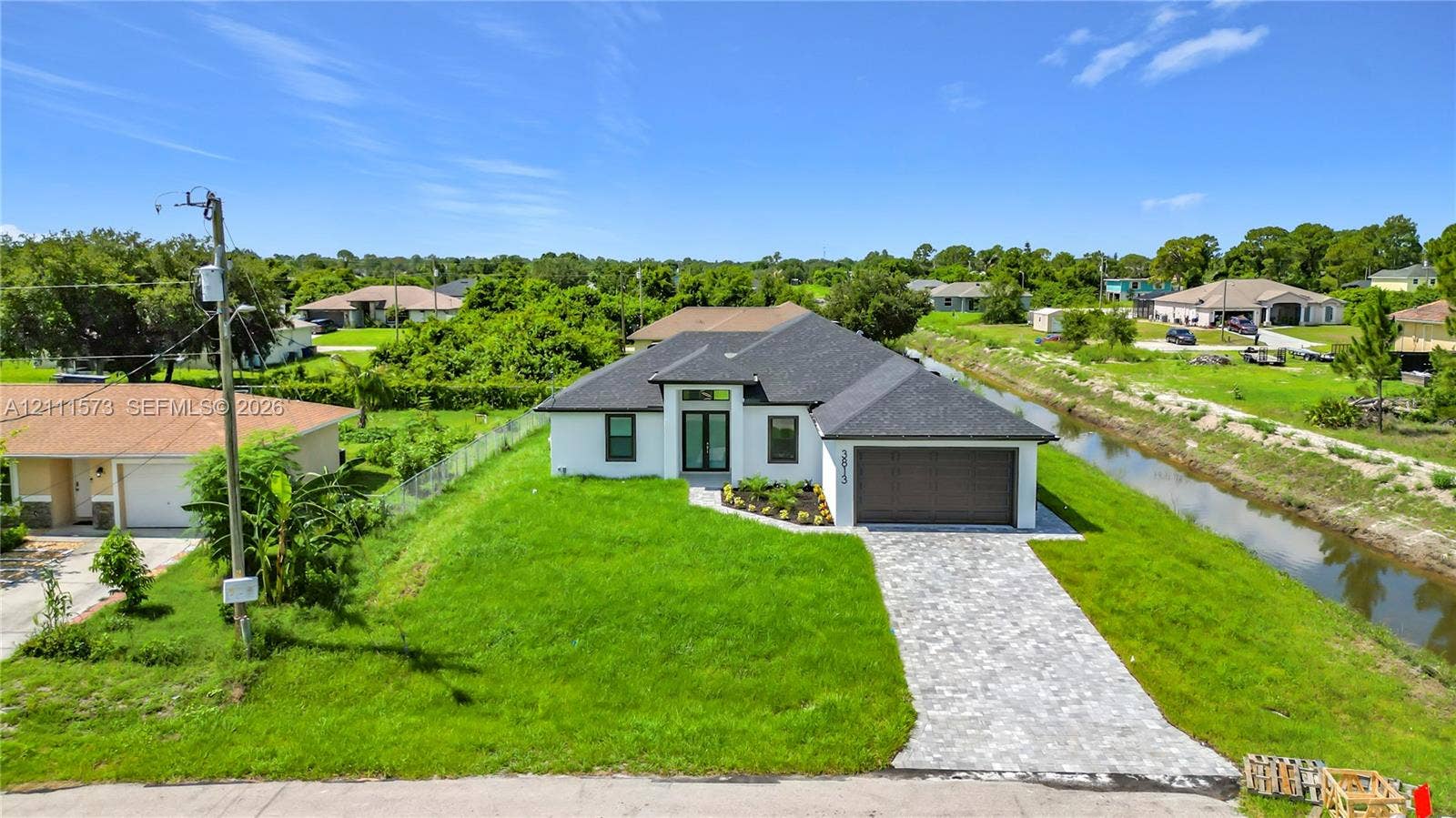 3813 SW 26th Street, Lehigh Acres, FL 33976 Single-story residence featuring a crisp white exterior, dark shingle roof, expansive paver driveway, and an attached two-car garage