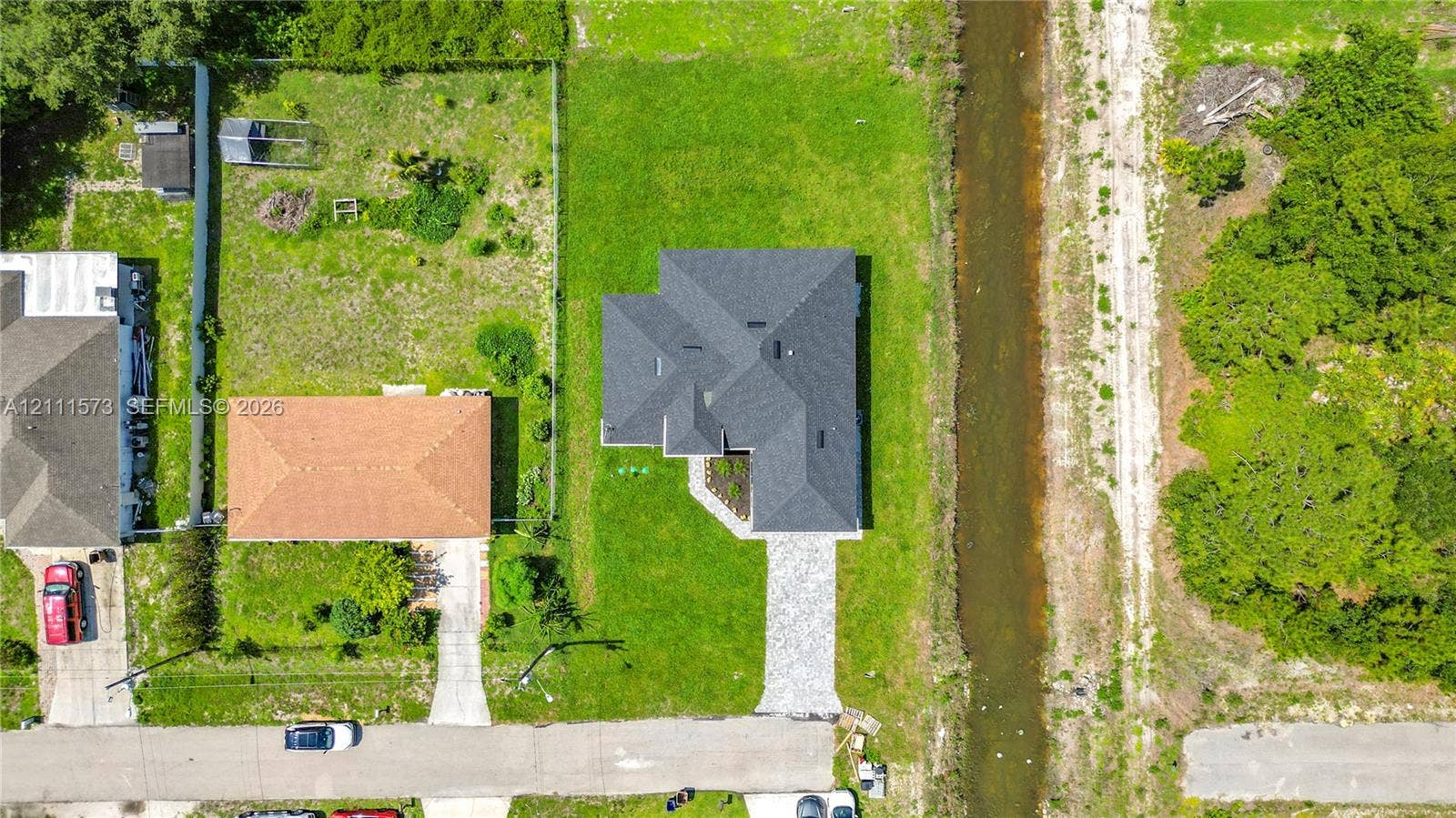 3813 SW 26th Street, Lehigh Acres, FL 33976 Aerial view featuring a multi-pitched asphalt shingle roof, paved concrete driveway, and expansive grass lot