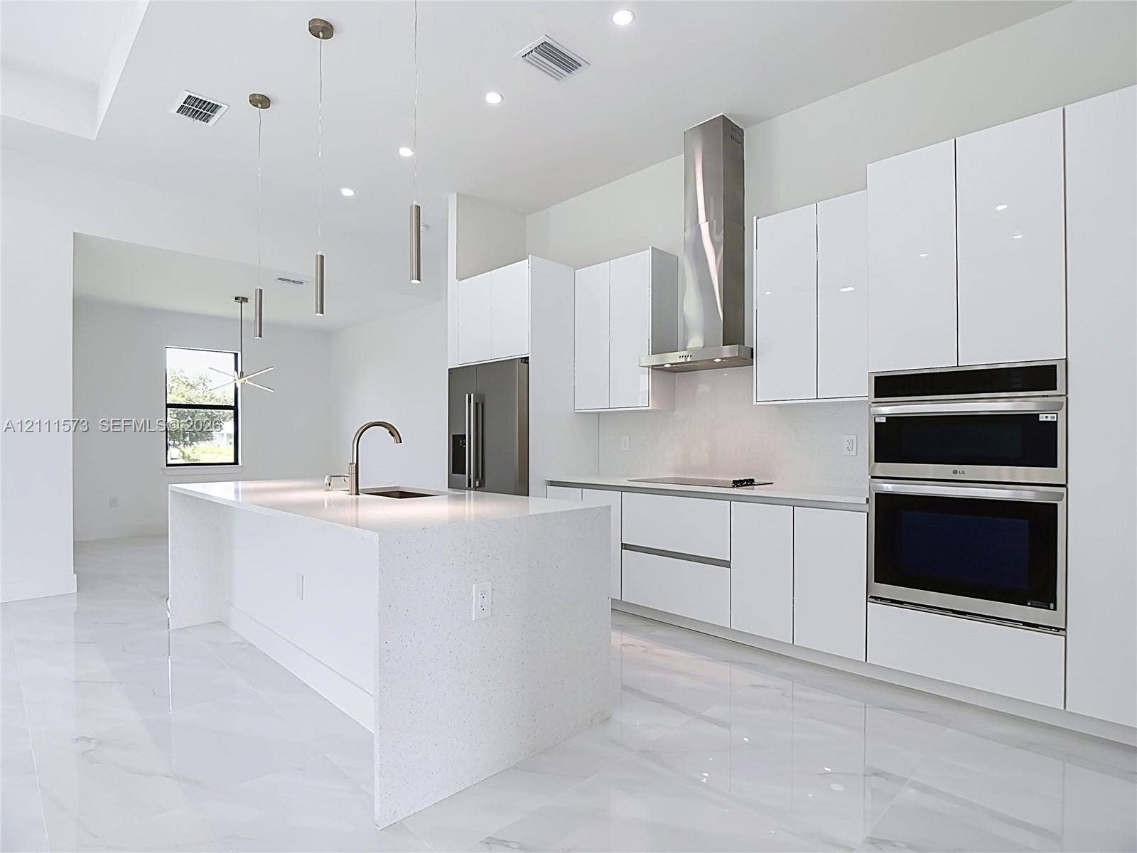 3813 SW 26th Street, Lehigh Acres, FL 33976 Modern kitchen featuring high-gloss cabinetry, stone-surface waterfall island with an undermount sink, built-in stainless steel double oven, stainless steel chimney range hood, and light-tone flooring