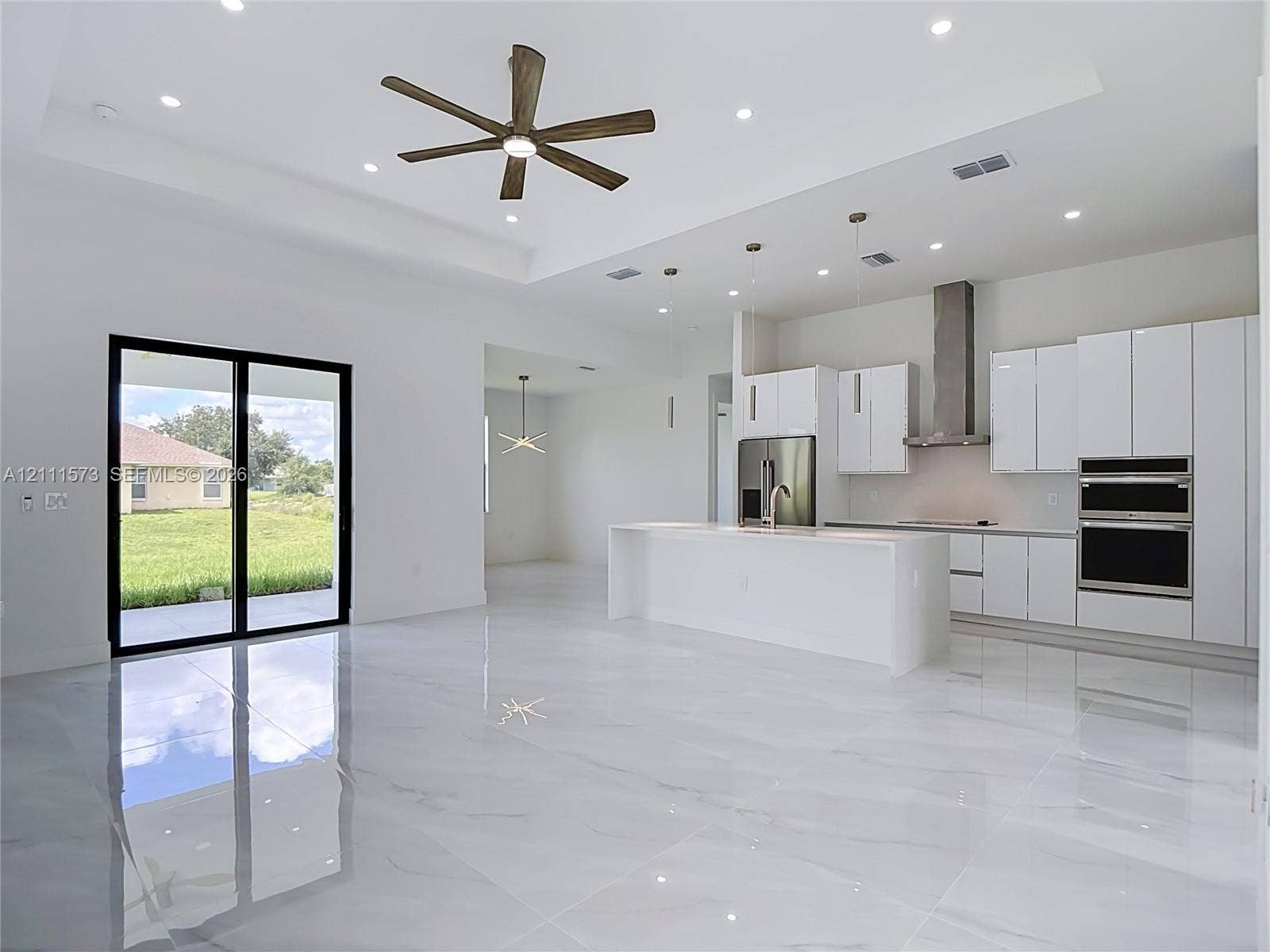 3813 SW 26th Street, Lehigh Acres, FL 33976 Open-concept living space featuring high tray ceilings, large-format polished tile flooring, white cabinetry, a center island with stone-finish countertops, and built-in stainless steel appliances
