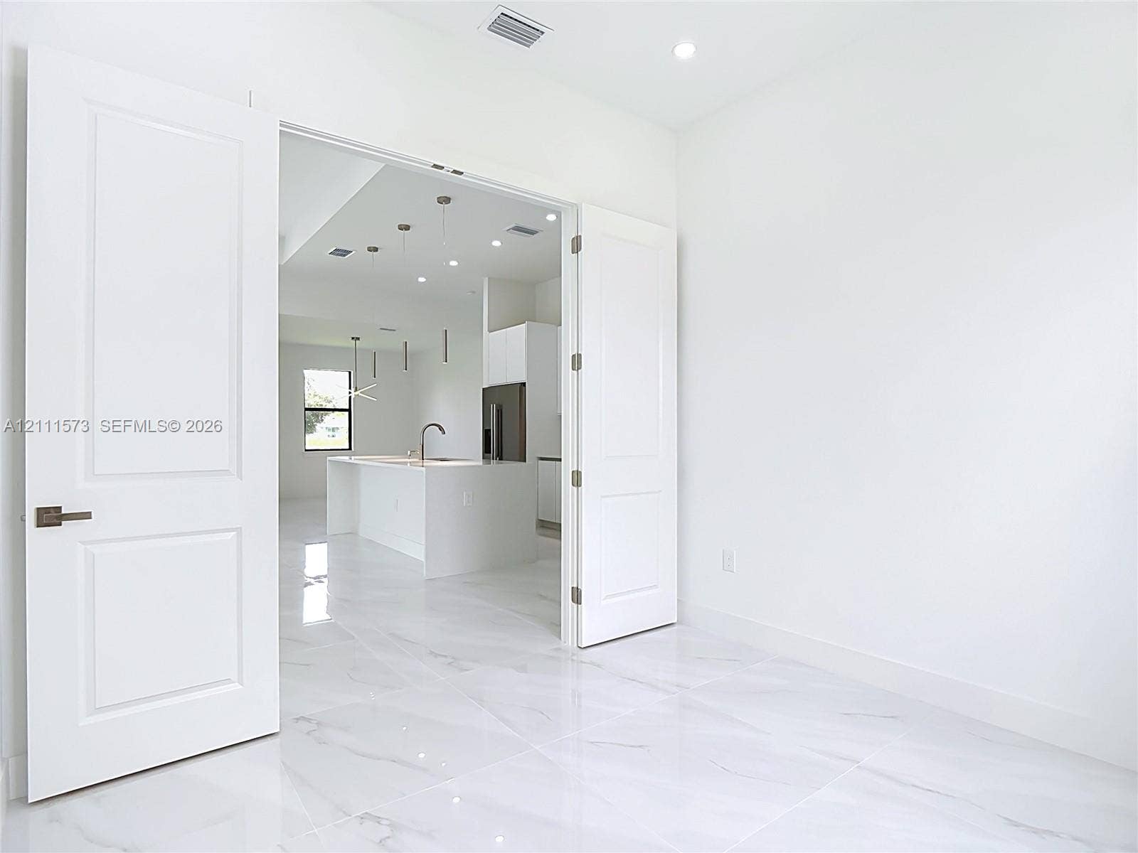 3813 SW 26th Street, Lehigh Acres, FL 33976 Interior space featuring large-format stone-finish tile flooring, white two-panel double doors with brushed nickel hardware, and recessed ceiling lighting