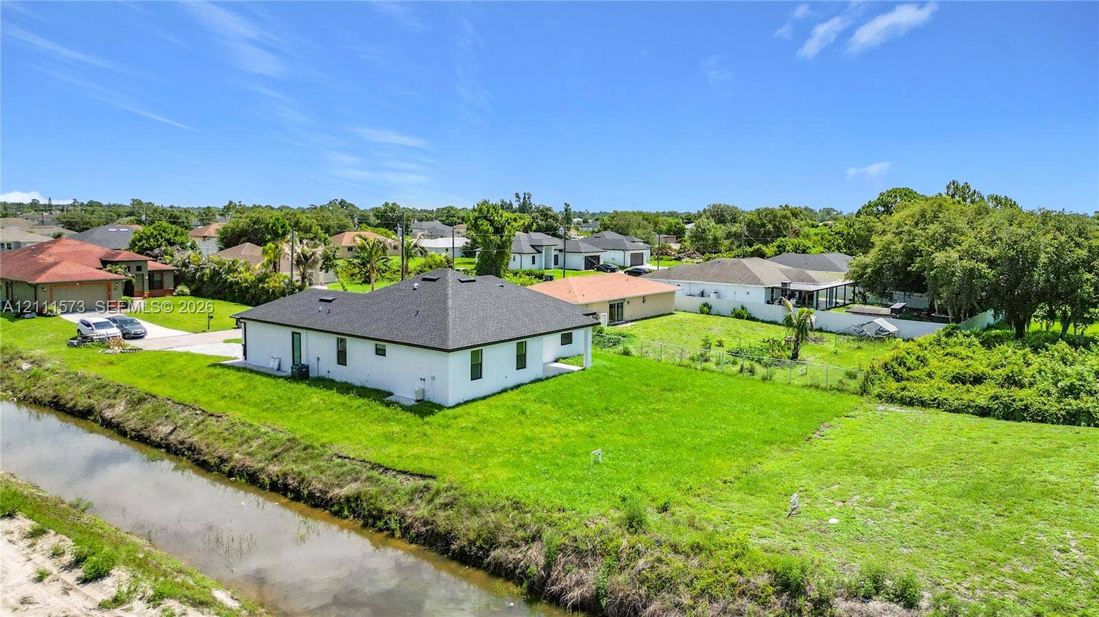 3813 SW 26th Street, Lehigh Acres, FL 33976 Single-story residence featuring a white exterior, dark shingle roof, expansive lot, and waterfront frontage