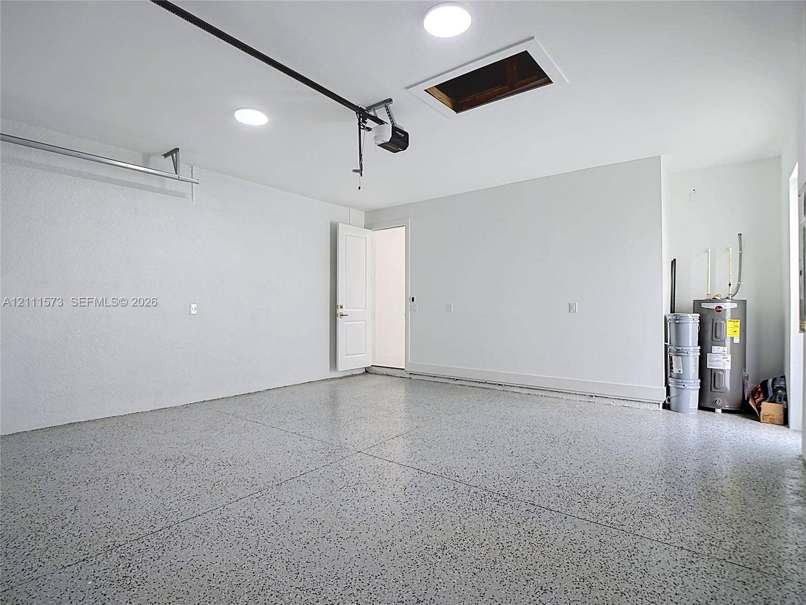3813 SW 26th Street, Lehigh Acres, FL 33976 Finished garage space featuring durable epoxy flooring, smooth white walls, recessed ceiling lighting, an automatic garage door opener, and a dedicated water heater