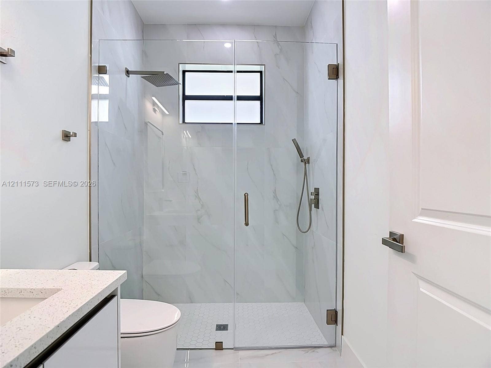 3813 SW 26th Street, Lehigh Acres, FL 33976 Walk-in shower featuring a frameless glass enclosure, rain-style shower head, handheld sprayer, and large-format wall tile with hexagonal floor tile