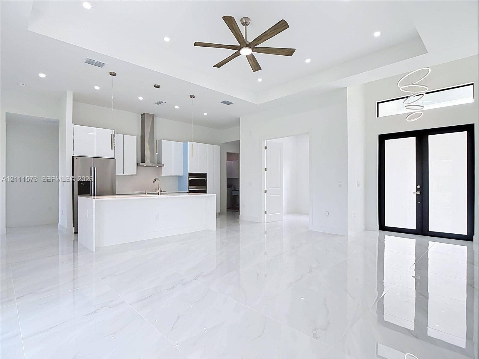 3813 SW 26th Street, Lehigh Acres, FL 33976 Open-concept kitchen featuring white cabinetry, a center island, stainless steel appliances, recessed ceiling lighting, and polished stone-finish flooring throughout