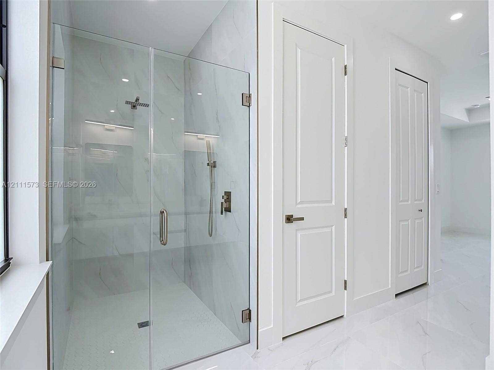 3813 SW 26th Street, Lehigh Acres, FL 33976 Walk-in shower featuring a frameless glass enclosure, floor-to-ceiling large-format tile surround, rainfall showerhead, handheld sprayer, and polished metallic fixtures