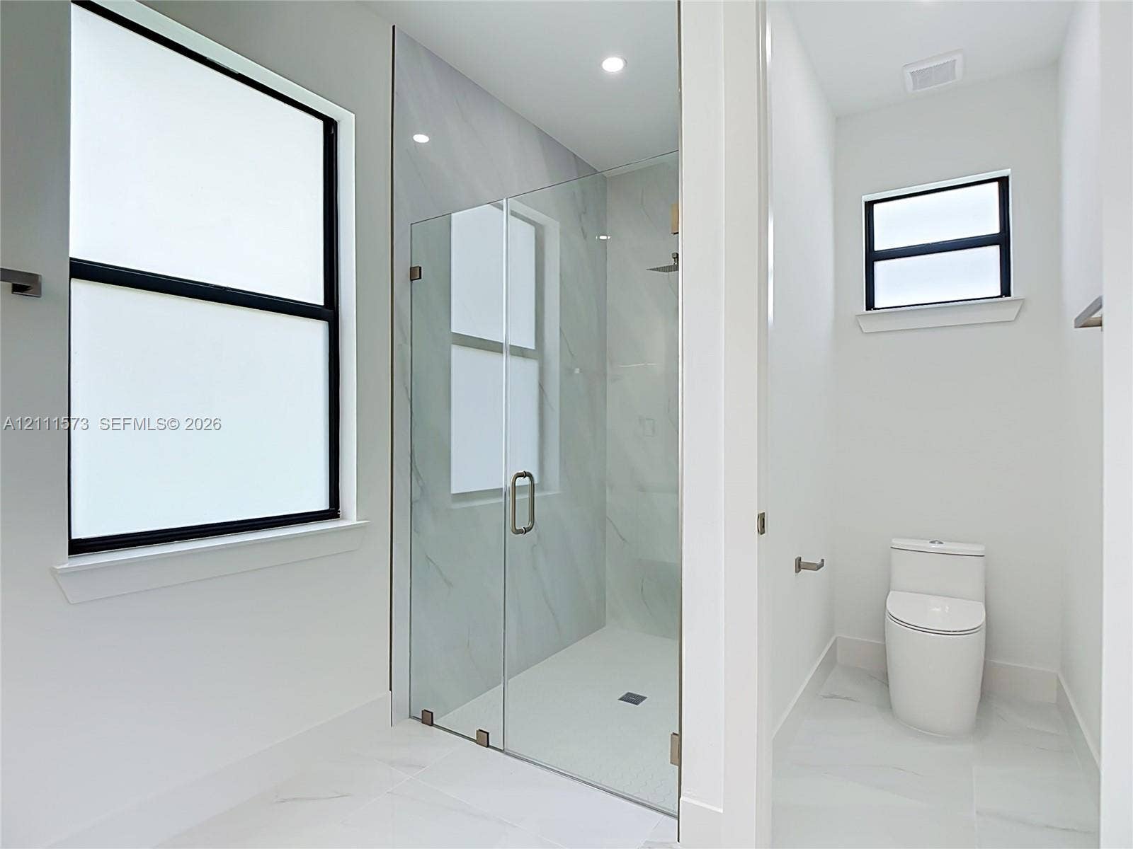 3813 SW 26th Street, Lehigh Acres, FL 33976 Walk-in shower featuring glass enclosure, stone-finish wall tile, and recessed lighting, accompanied by a low-profile toilet and black-framed windows