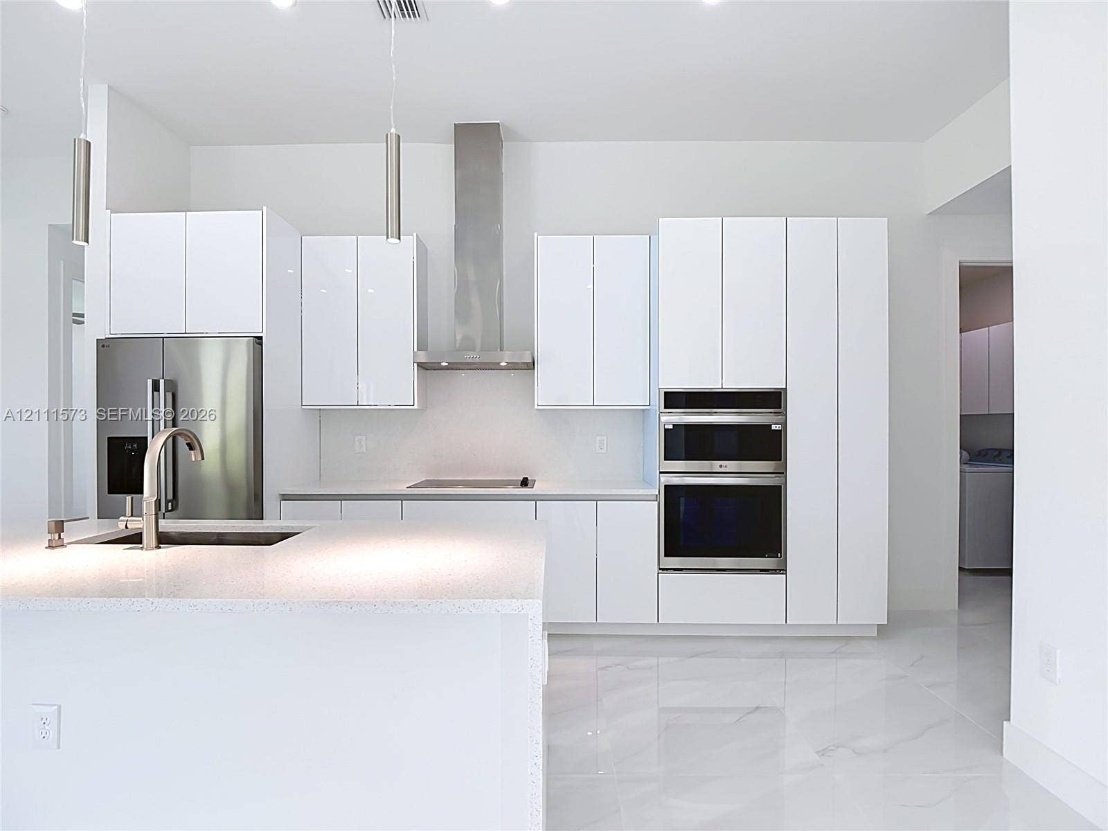 3813 SW 26th Street, Lehigh Acres, FL 33976 Kitchen featuring white high-gloss cabinetry, stainless steel built-in double ovens and range hood, center island with stone-surface countertop, and large-format porcelain floor tile