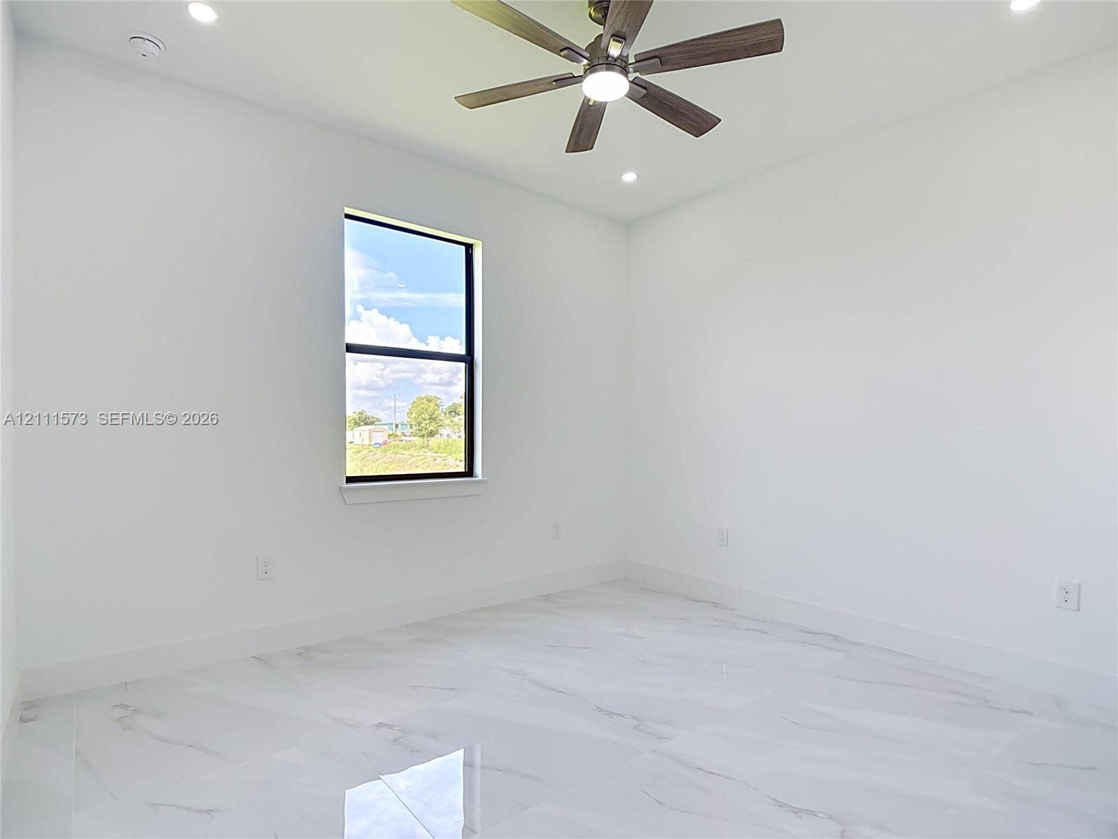 3813 SW 26th Street, Lehigh Acres, FL 33976 Neutral-toned interior space featuring white-finish tile flooring, recessed lighting, a ceiling fan with integrated lighting, and a single-pane window with a black frame
