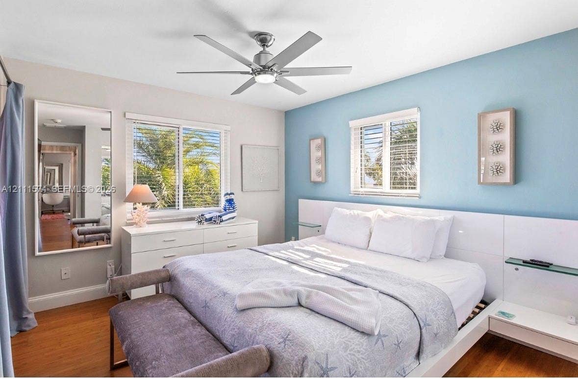 Bedroom featuring wood-finish flooring, a contemporary six-blade ceiling fan with integrated lighting, and a built-in white panel headboard with glass shelving