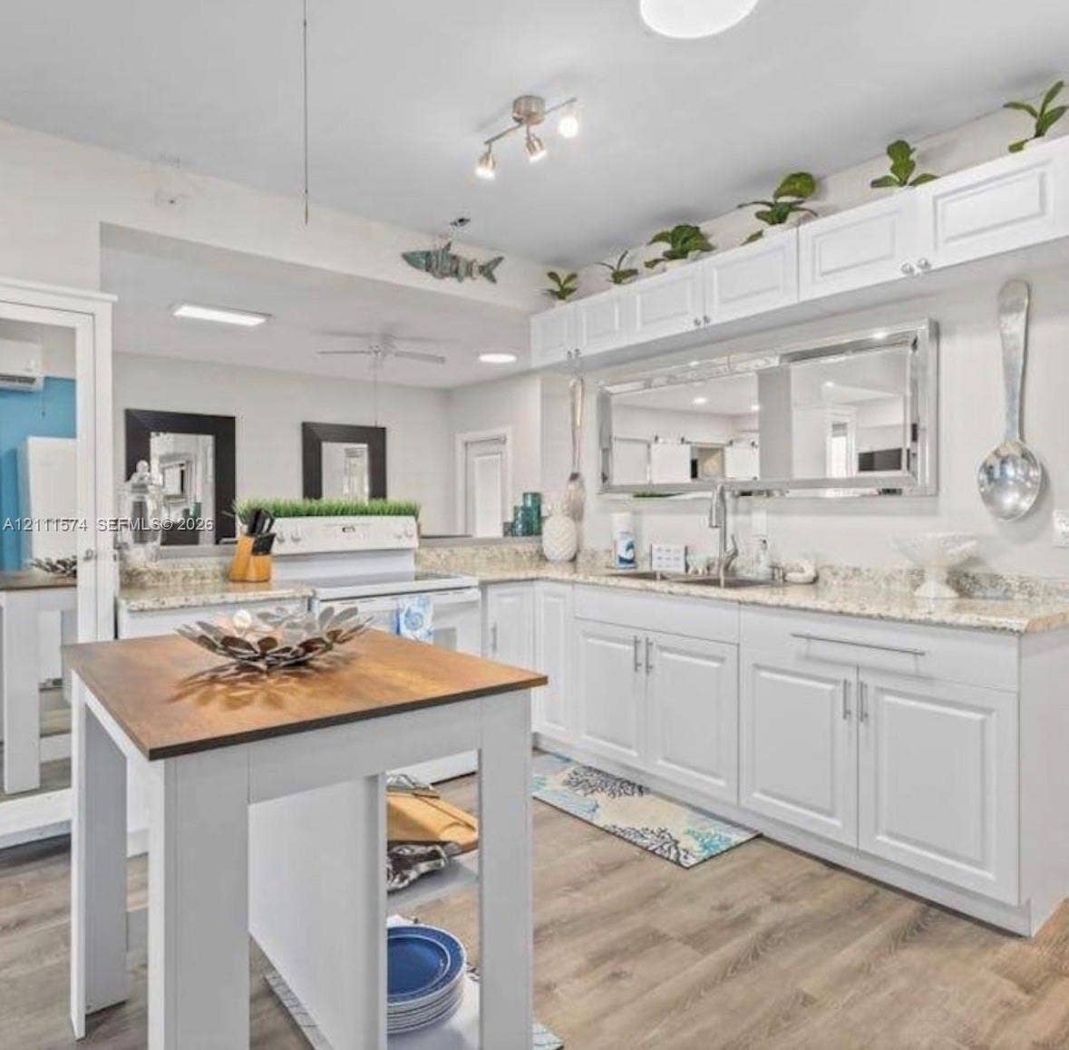Kitchen featuring white shaker-style cabinetry, stone-finish countertops, wood-finish flooring, a stainless steel undermount sink, and a center island with a wood-tone surface