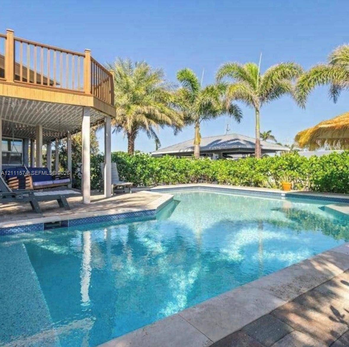 In-ground swimming pool with tile border, elevated wood-finish deck, stone paver pool deck, and mature palm trees