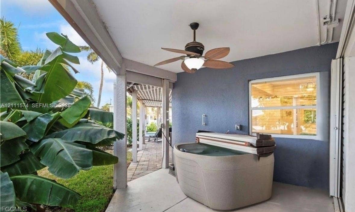 Covered patio featuring a ceiling-mounted light and fan fixture, portable spa, masonry wall finish, and paver walkway