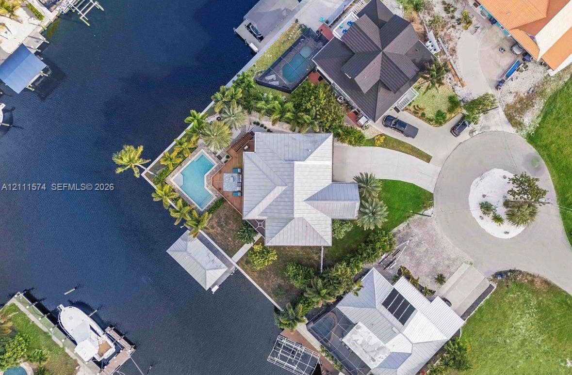 Waterfront property featuring a private swimming pool, concrete boat dock, and a paved circular driveway