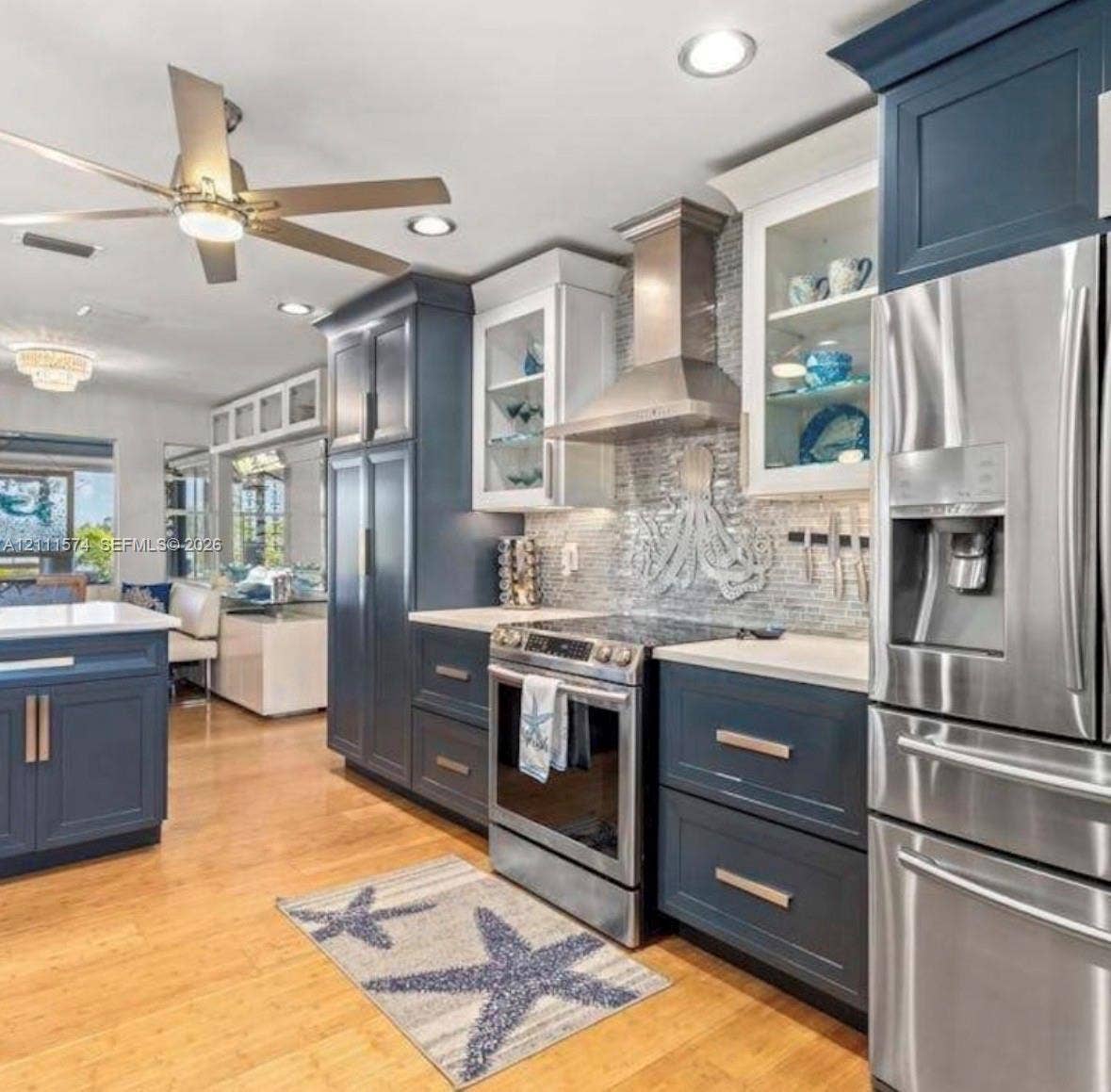 Kitchen featuring dual-toned navy and white cabinetry, stone-finish countertops, stainless steel appliances, a tile backsplash, and wood-finish flooring