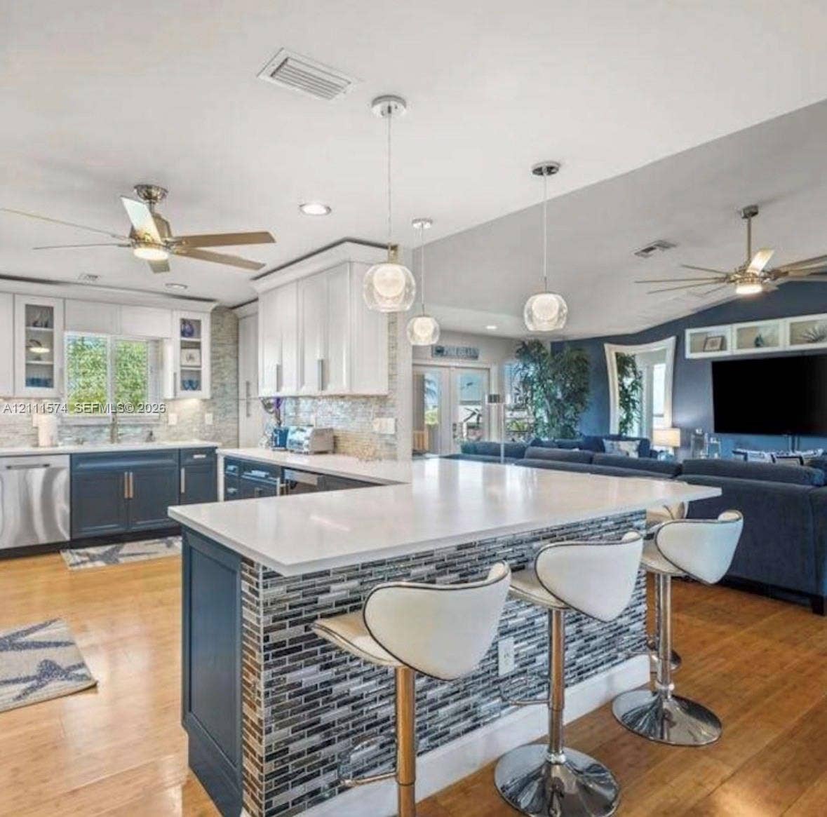 Kitchen featuring white shaker-style cabinetry, a quartz-topped island with mosaic tile inlay, glass globe pendant lighting, stainless steel appliances, and wood-finish flooring