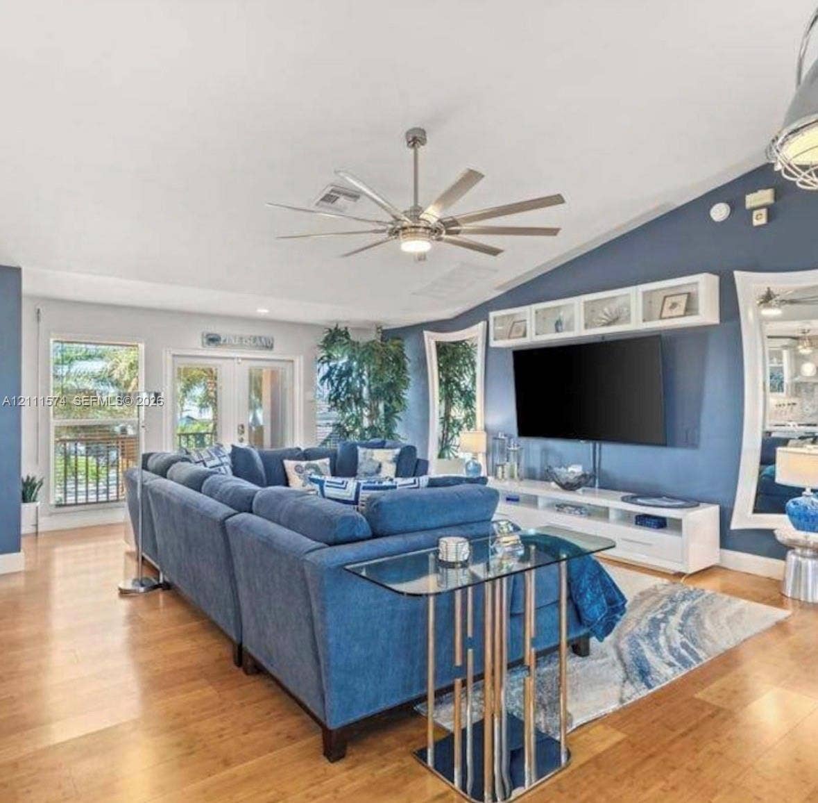 Vaulted ceiling featuring a multi-blade ceiling fan, expansive wood-finish flooring, and built-in upper wall cabinetry