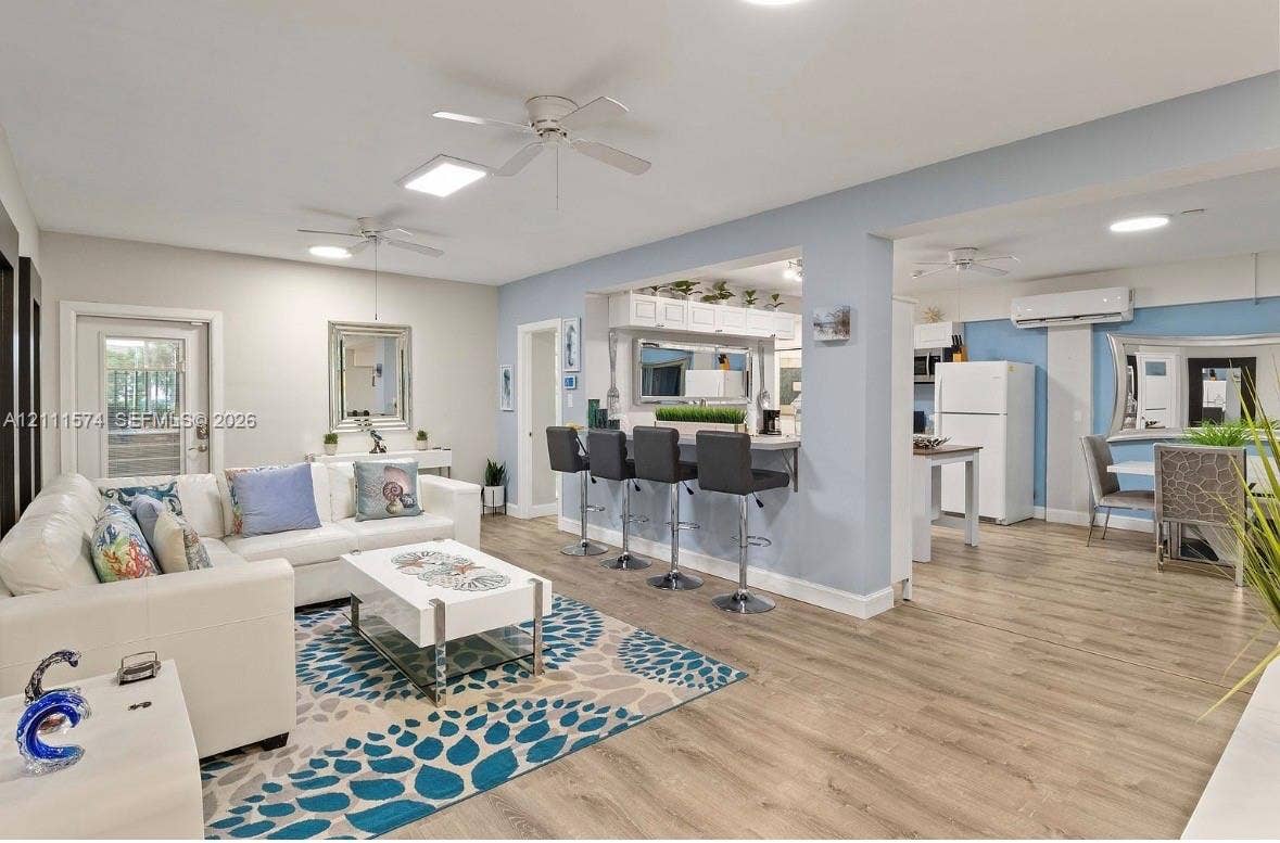 Open-concept interior featuring wood-finish flooring, a kitchen pass-through counter, ceiling fans, and a ductless mini-split system