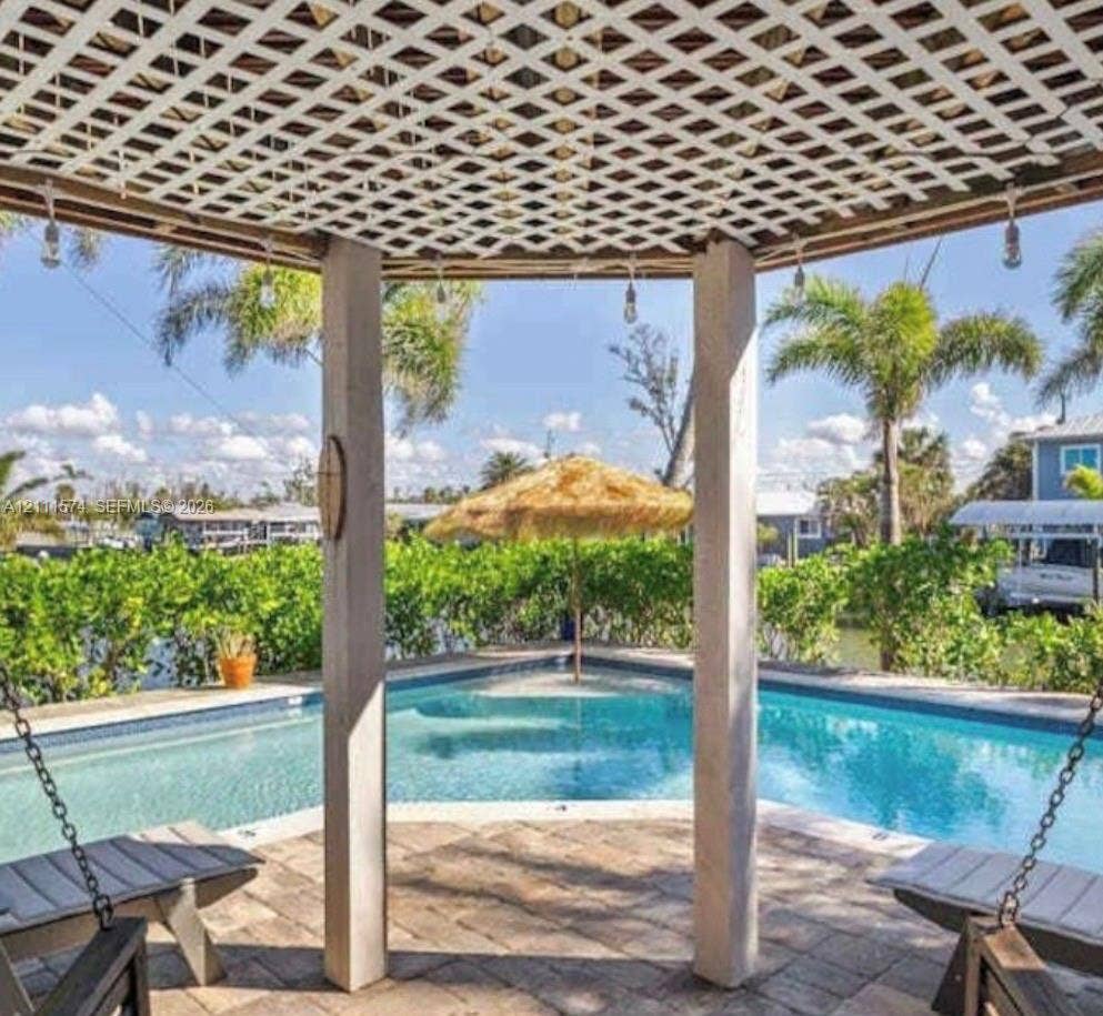 Covered gazebo featuring a lattice roof, stone paver flooring, and suspended bench seating, positioned over a swimming pool with water access