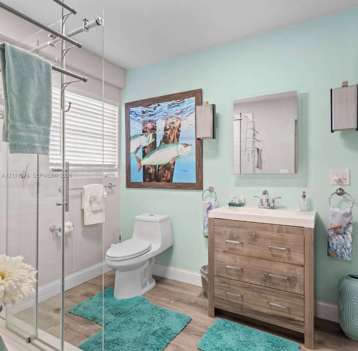 Bathroom featuring wood-finish flooring, a wood-grain vanity with a white countertop, a frameless glass-enclosed shower, and wall-mounted rectangular lighting fixtures