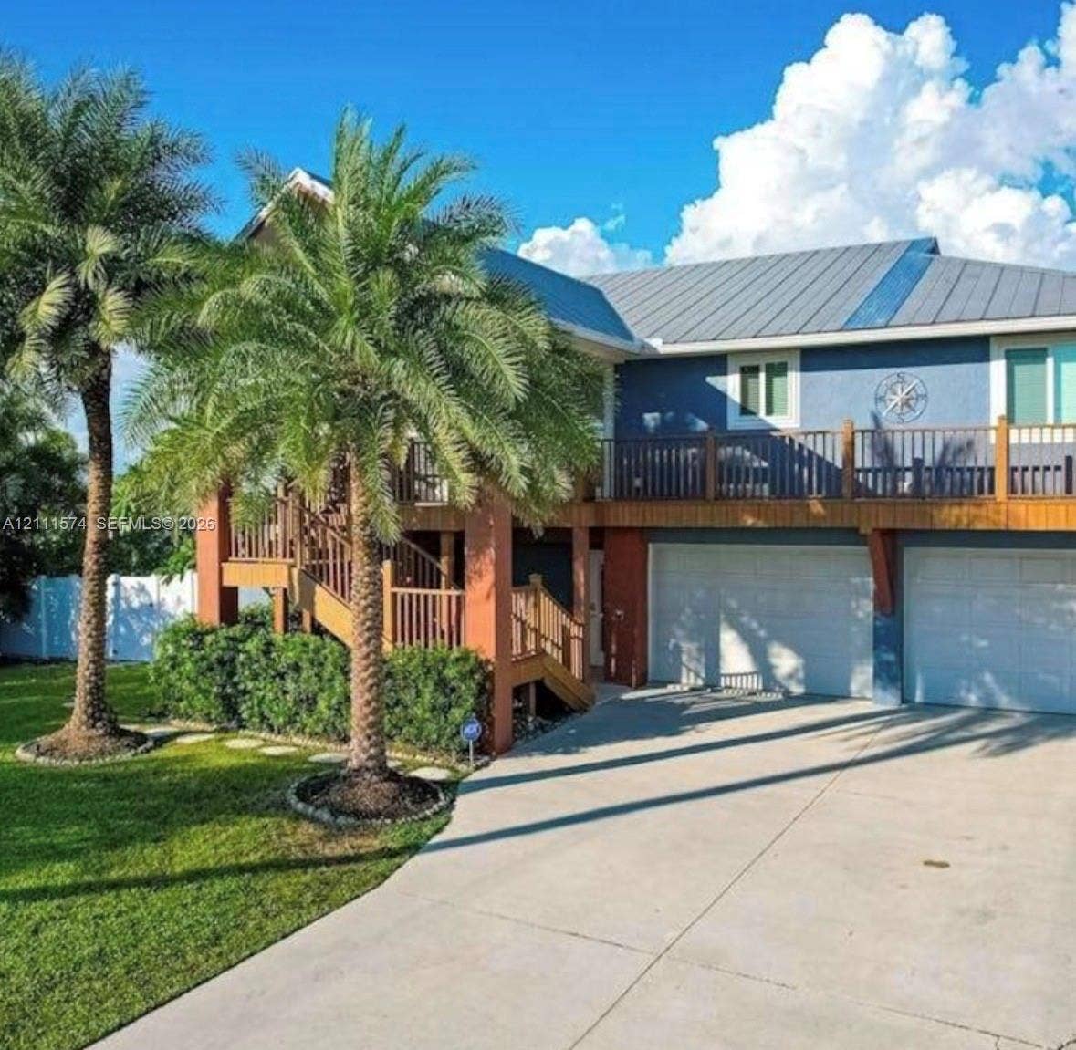 Two-story exterior featuring a metal roof, wraparound wooden deck, dual-bay garage, and concrete driveway