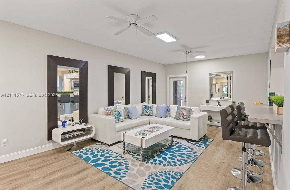 Living area featuring wood-finish flooring, two ceiling fans, recessed lighting, and three wall-mounted, dark-framed mirrors