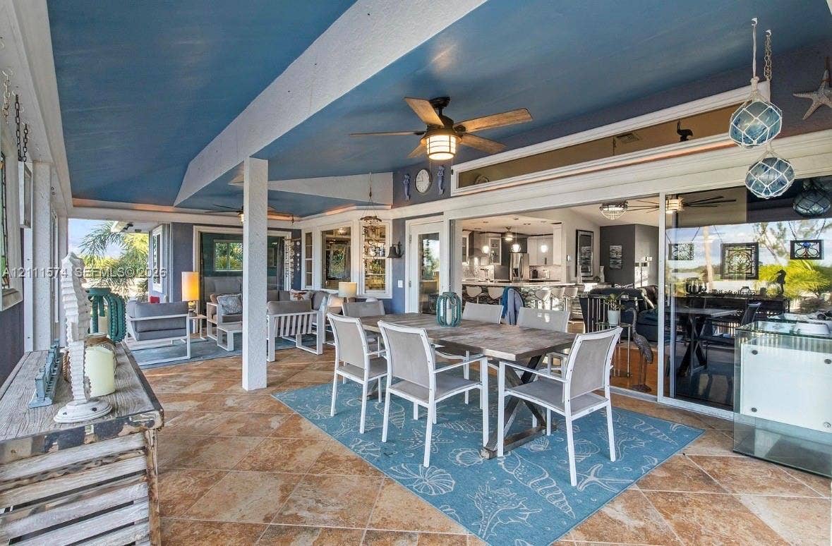 Covered patio featuring stone-finish flooring, a painted tray ceiling, a dual-blade ceiling fan, and large-format sliding glass doors