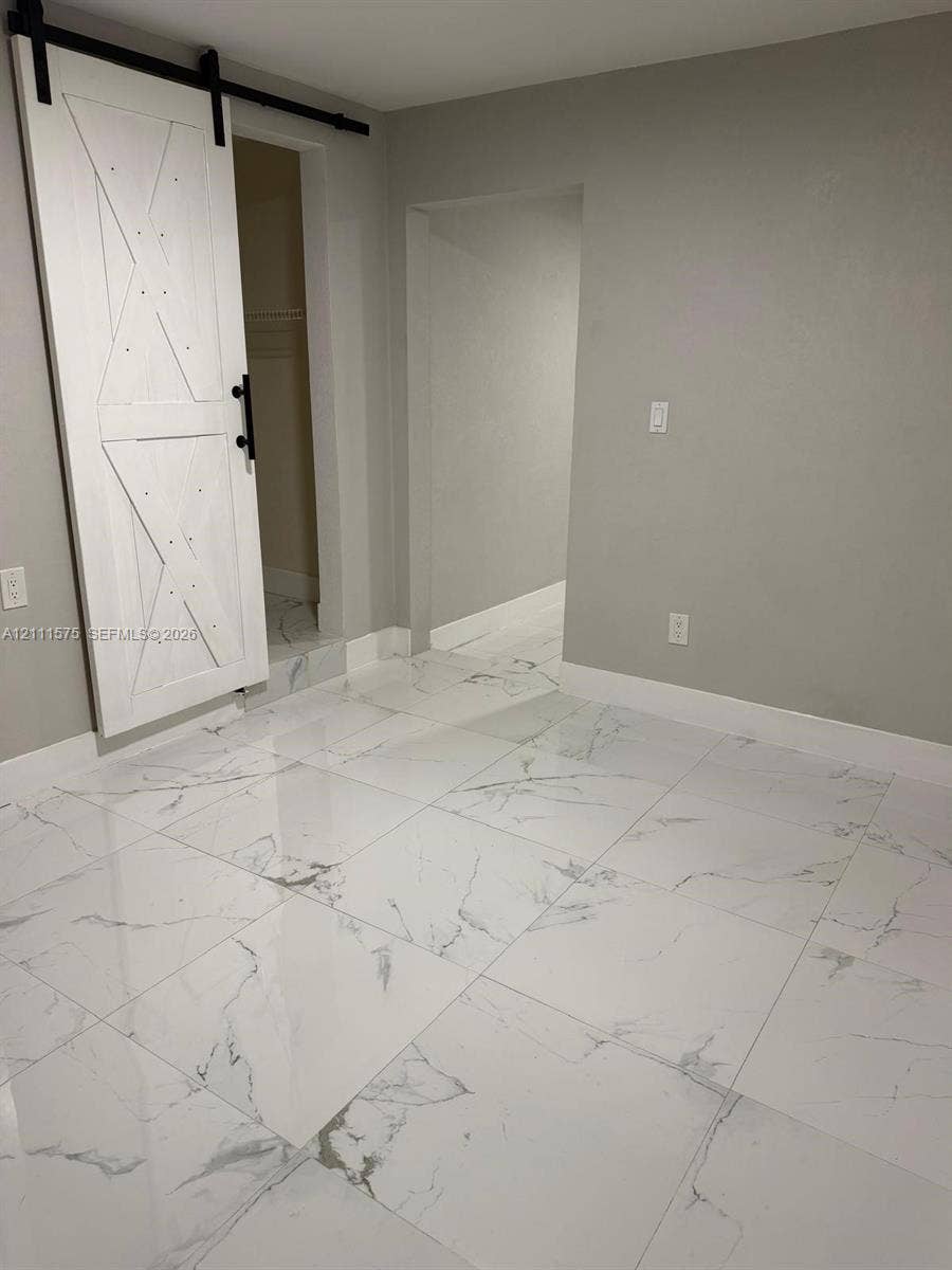 Large-format polished tile flooring featuring a grey-vein pattern, white wood-finish sliding barn door with black iron hardware, and neutral wall tones