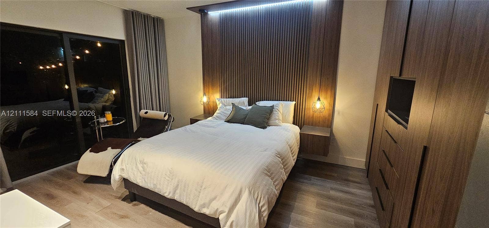Wood-finish flooring, floor-to-ceiling wood-slat accent wall with integrated ambient lighting, suspended bedside cabinetry, and built-in floor-to-ceiling cabinetry