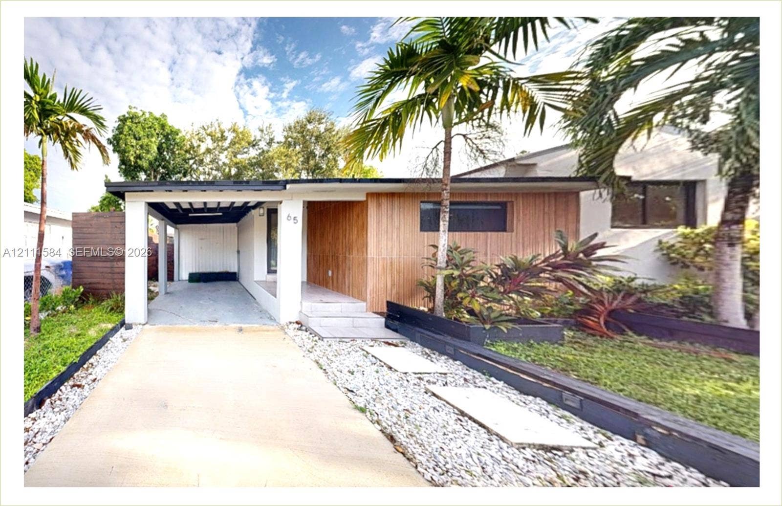 Mid-century modern facade featuring vertical wood panel siding, a covered carport, concrete driveway with integrated stone landscape borders, and a stepped entry walkway