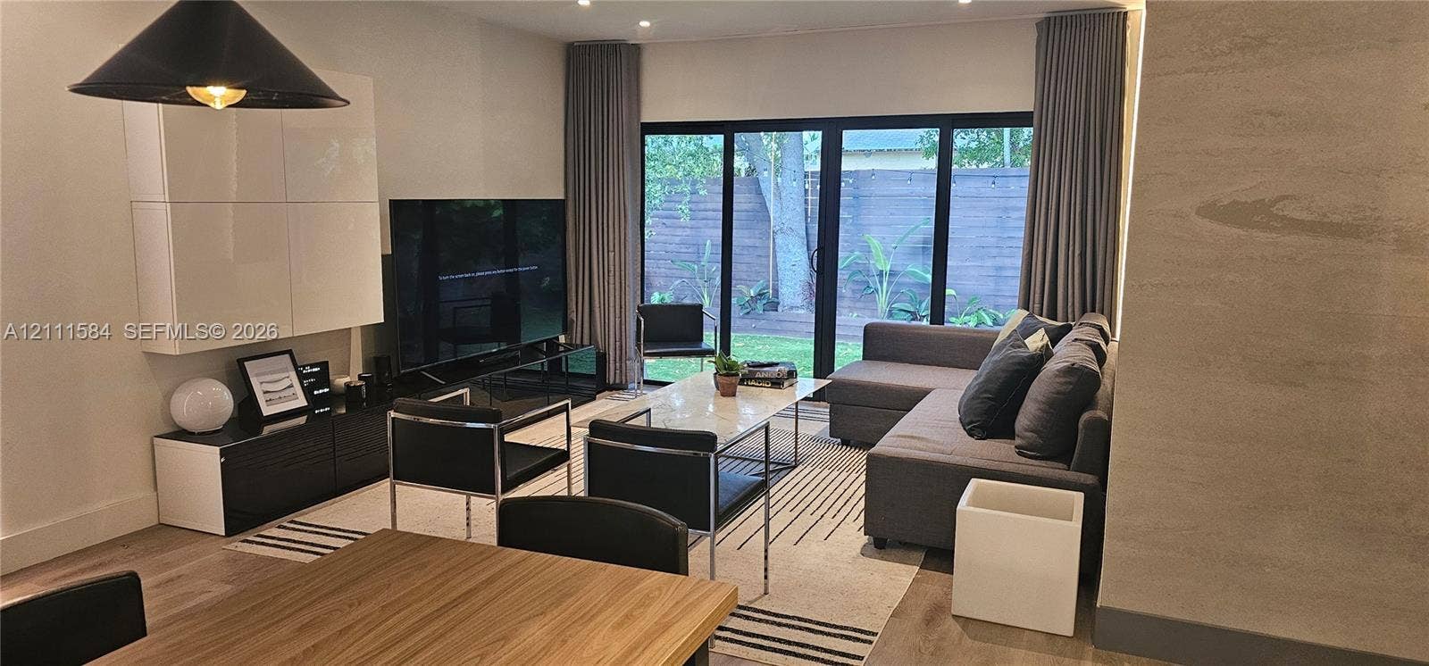 Living area featuring wood-finish flooring, floor-to-ceiling black-framed glass sliding doors, wall-mounted white cabinetry, recessed lighting, and a textured accent wall