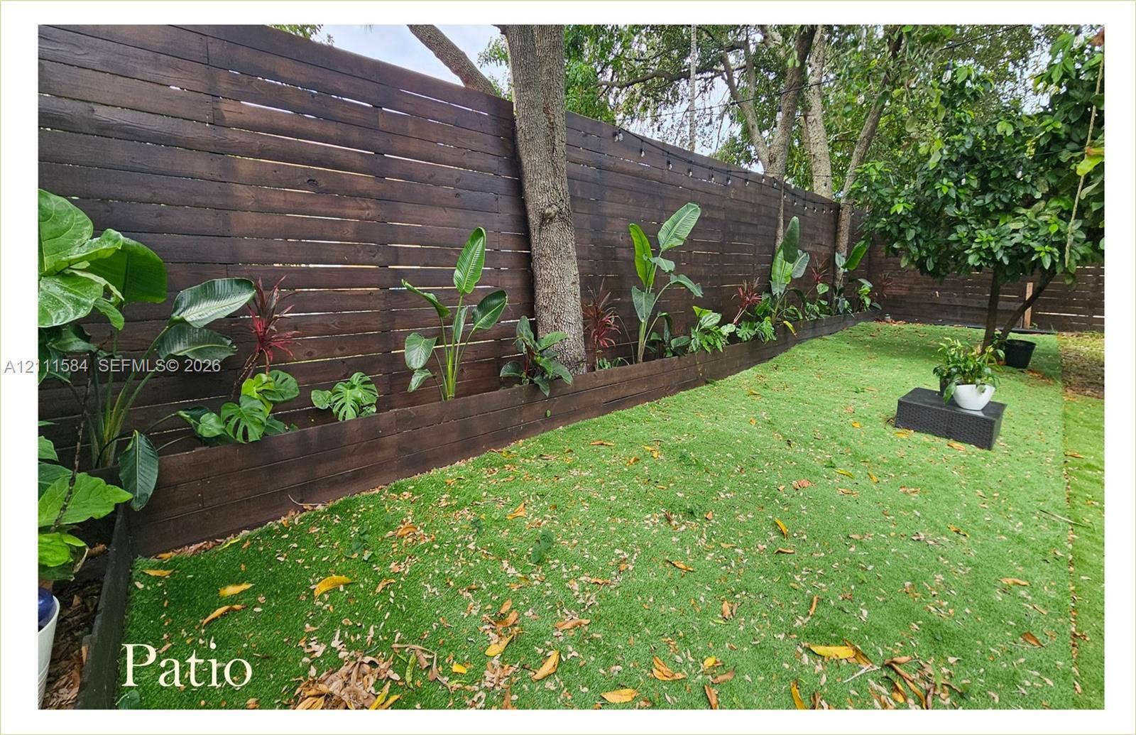 Horizontal dark-stained wood slat fencing, artificial turf lawn, raised wood garden bed border, and mature trees