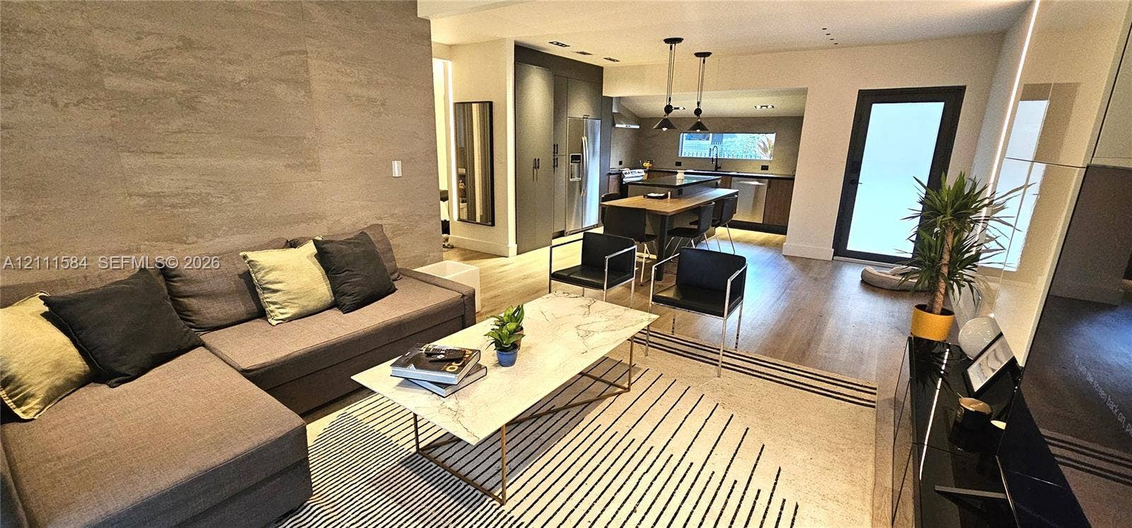Open-concept area featuring textured stone-look accent wall, wood-finish flooring, recessed lighting, and kitchen with integrated cabinetry and island