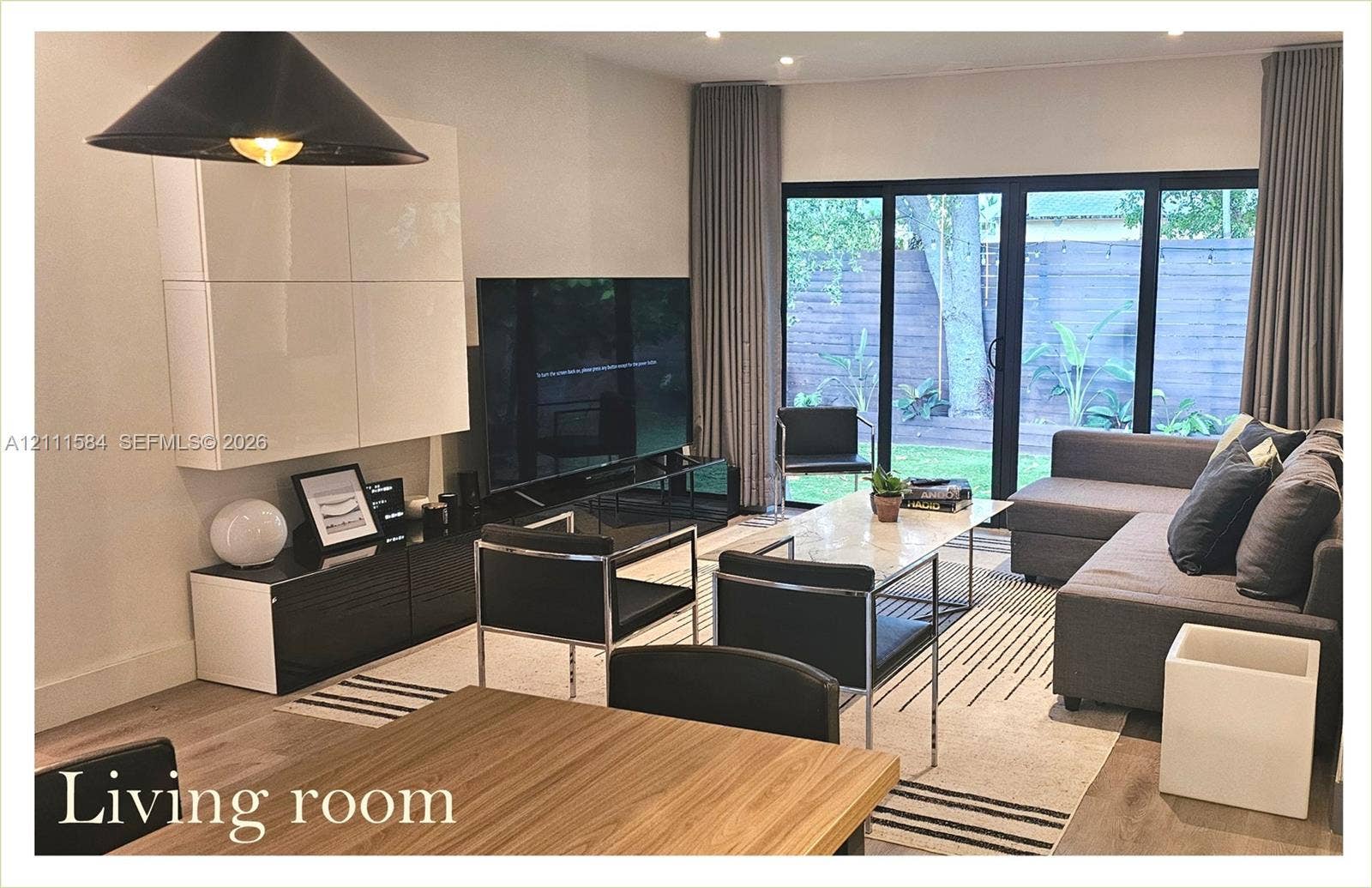 Living area featuring wood-finish flooring, recessed lighting, matte black industrial pendant fixture, and floor-to-ceiling black-framed sliding glass doors